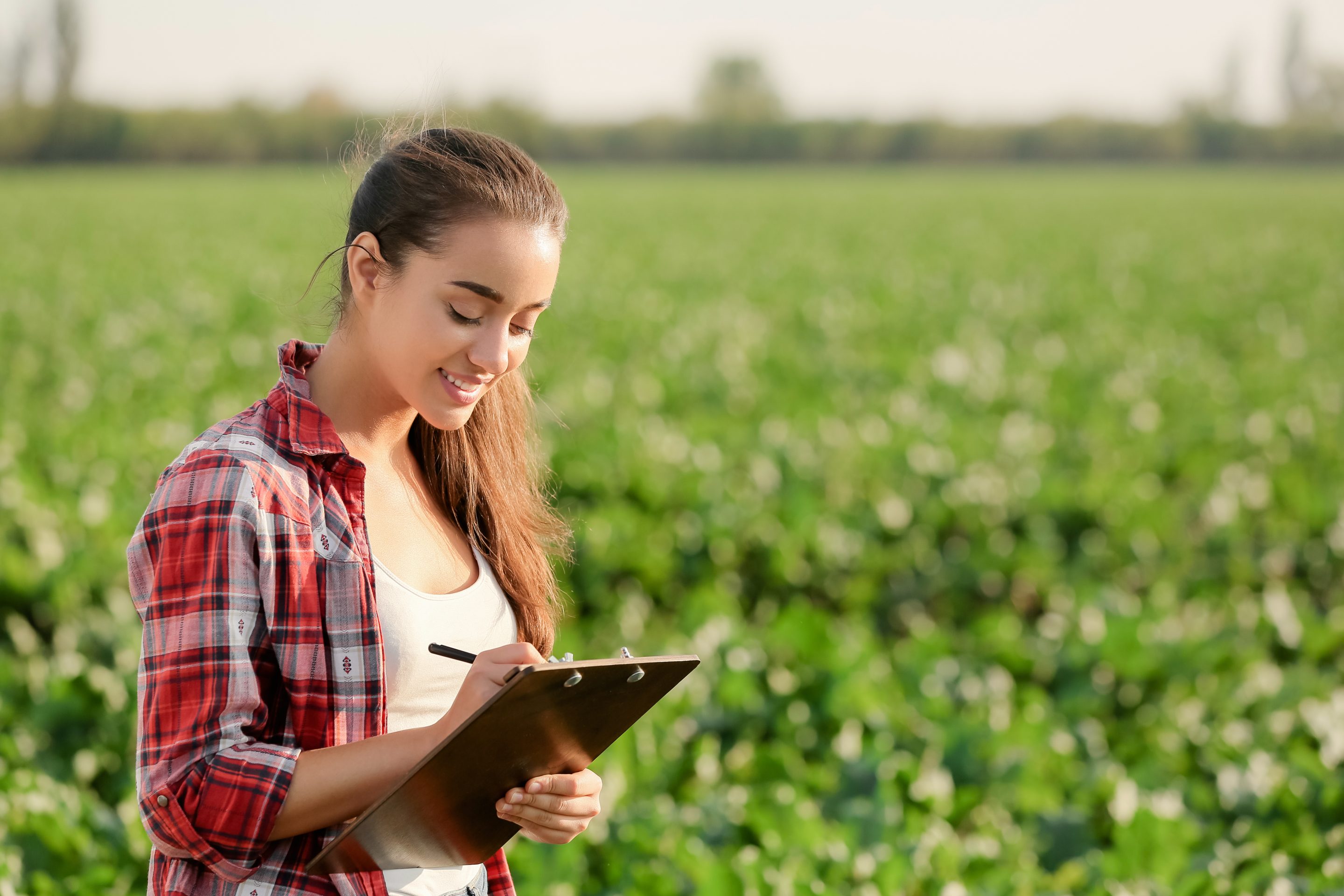A woman writing down notes on a clipboard while standing in a field.